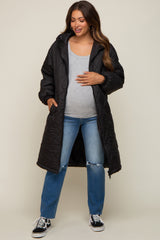 woman wearing a black long quilted maternity coat over a gray top and blue jeans, gently holding her baby bump