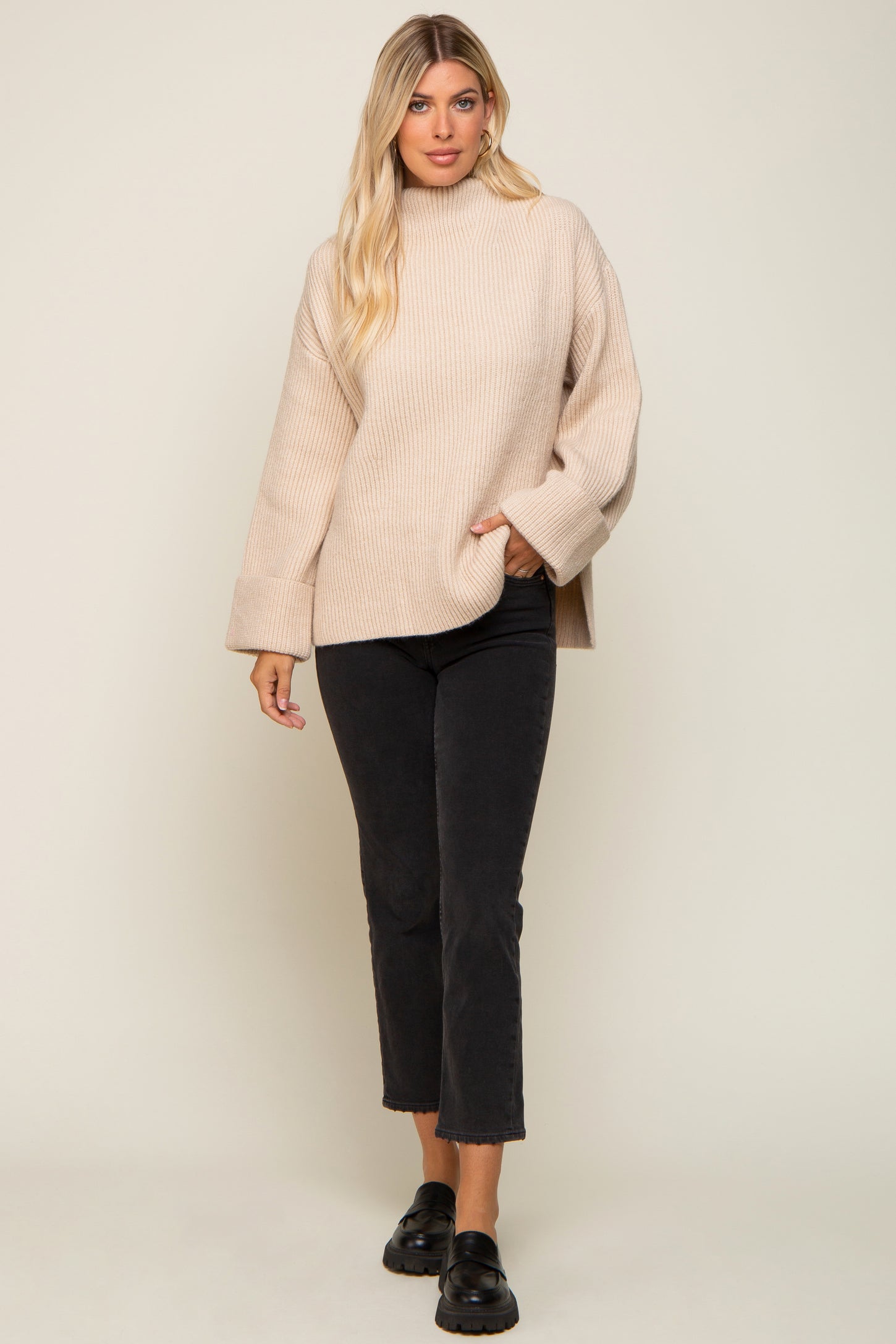 Woman wearing a beige oversized ribbed turtleneck sweater and black cropped jeans with loafers
