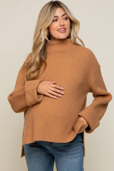 Pregnant woman wearing a camel-colored ribbed mock neck maternity sweater and blue jeans