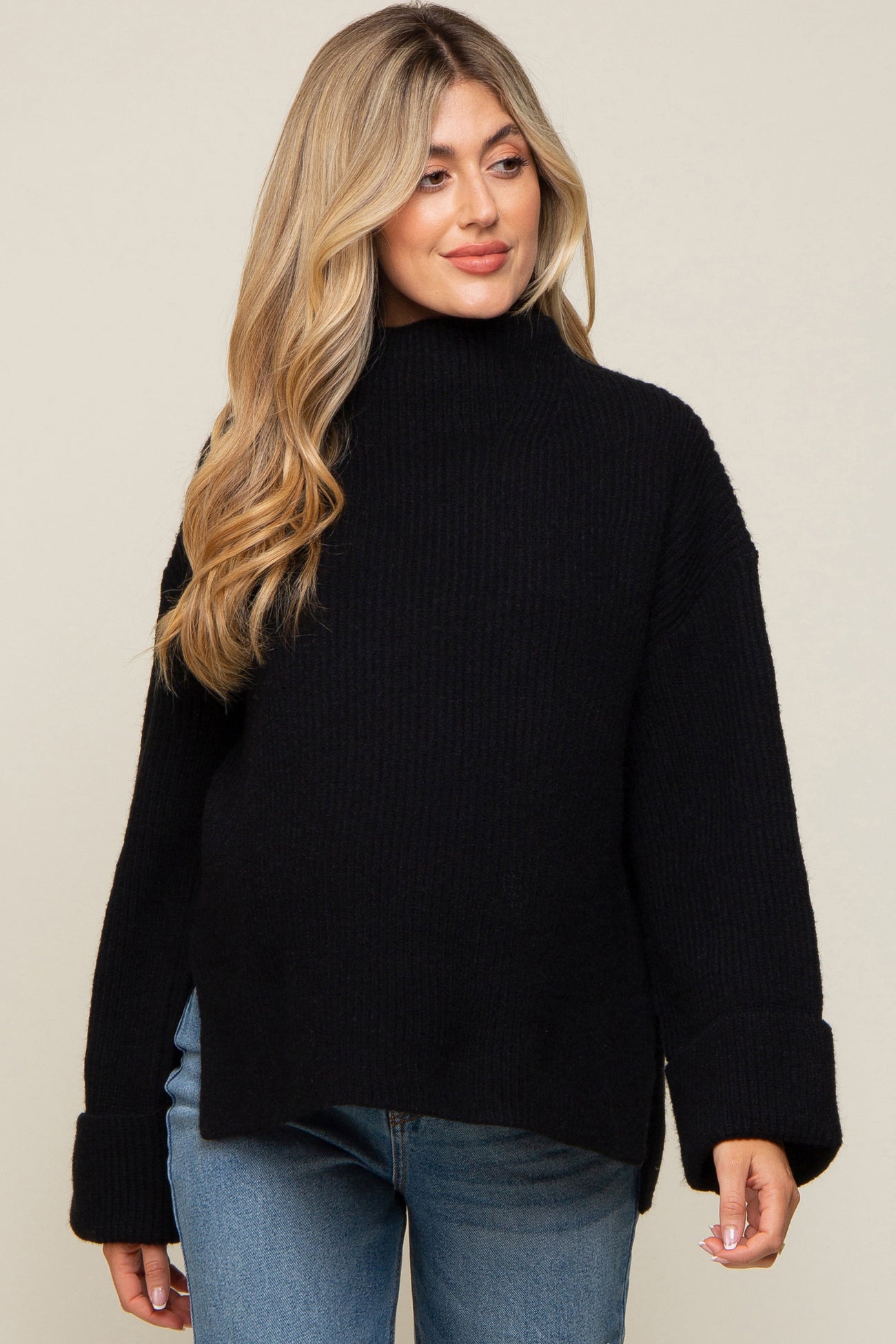 woman wearing a black oversized maternity sweater with a high neck and wide cuffs, styled with blue jeans