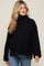 woman wearing a black oversized maternity sweater with a high neck and wide cuffs, styled with blue jeans