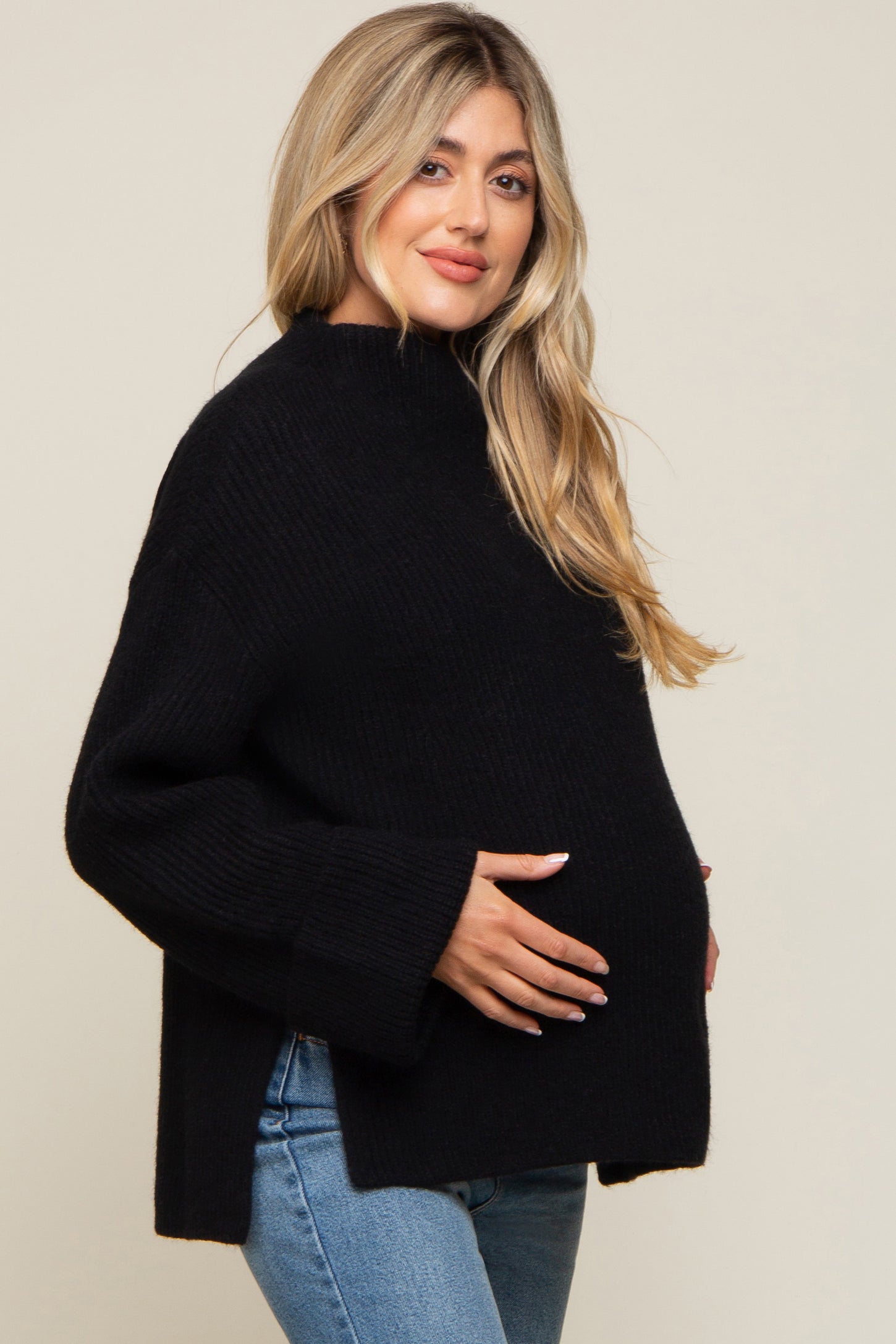 woman wearing a black maternity sweater with a relaxed fit, cradling her baby bump, paired with light blue jeans