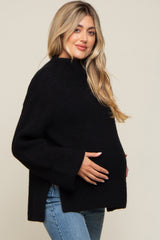 woman wearing a black maternity sweater with a relaxed fit, cradling her baby bump, paired with light blue jeans