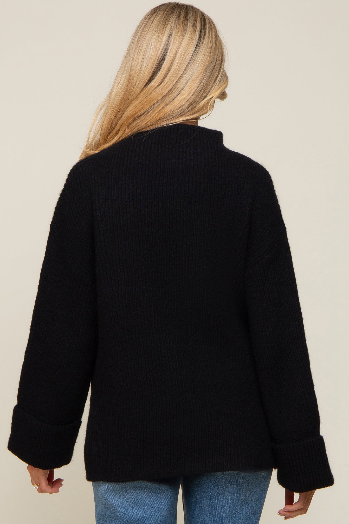 woman wearing a black oversized maternity sweater with a high neck and wide cuffs, viewed from the back