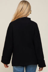 woman wearing a black oversized maternity sweater with a high neck and wide cuffs, viewed from the back