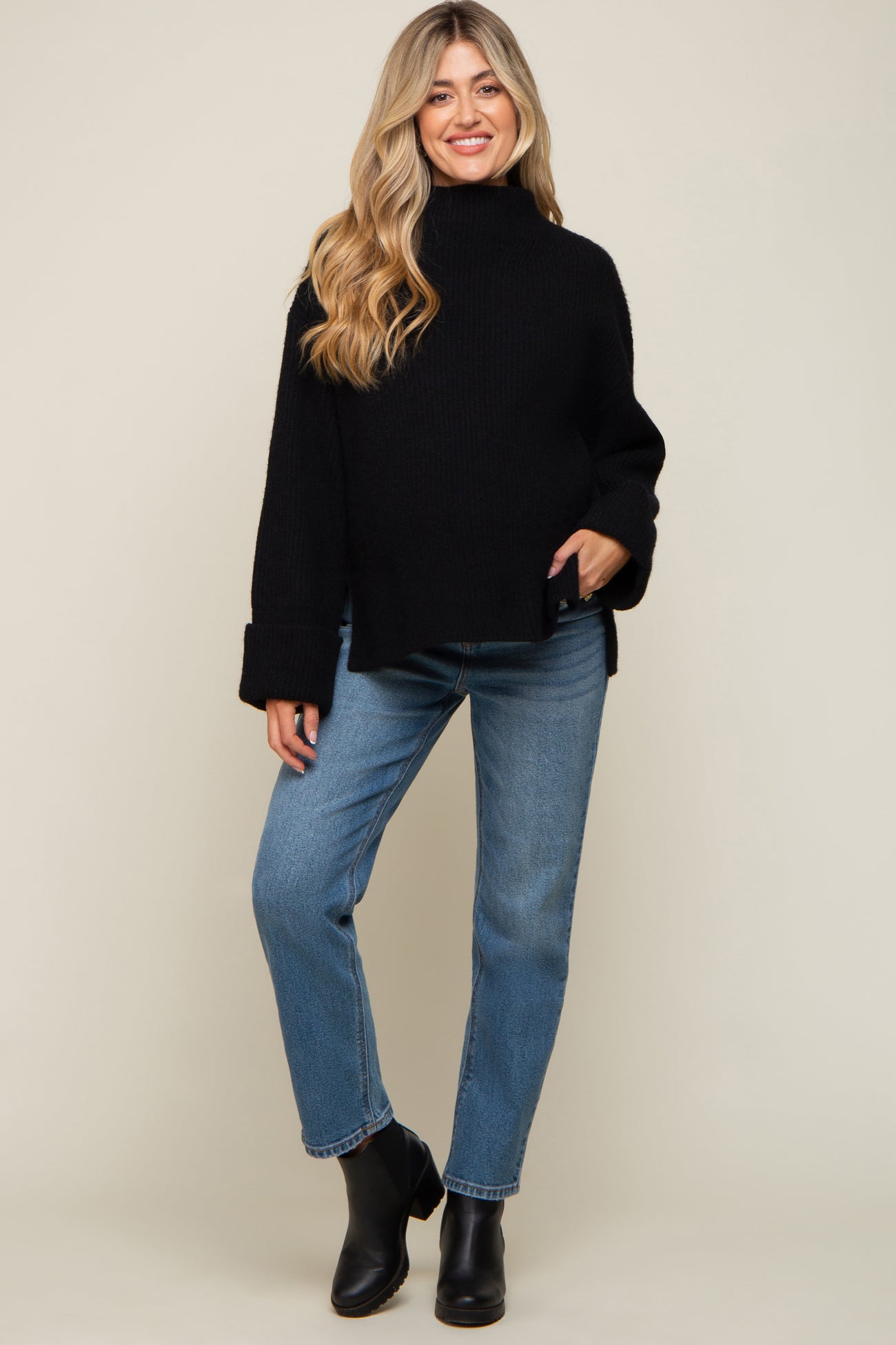 woman wearing a black oversized knit maternity sweater with wide sleeves and blue jeans, standing and smiling