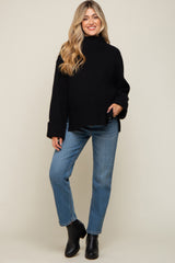 woman wearing a black oversized knit maternity sweater with wide sleeves and blue jeans, standing and smiling