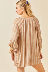 Woman wearing a tan and white geometric print tunic dress with long sleeves and pockets