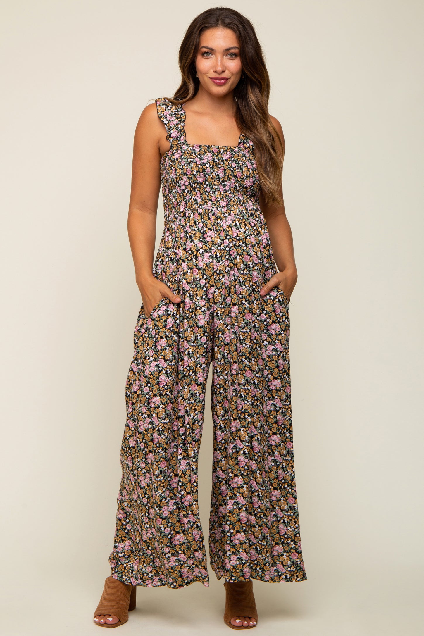 woman wearing a floral maternity jumpsuit with wide legs and pockets, featuring a square neckline and ruffled straps