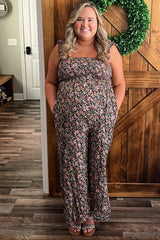 woman wearing a floral maternity jumpsuit with pockets and a baby bump, standing against a wooden door