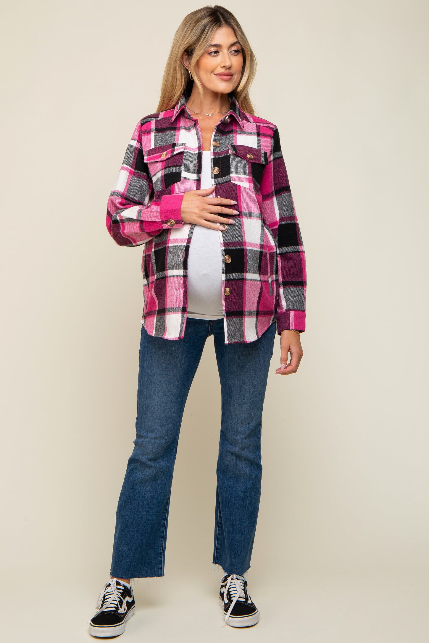 woman wearing a pink and black plaid maternity shirt and holding her baby bump, paired with blue flared jeans