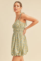 woman wearing a light green floral mini dress with tie straps and a smocked bodice