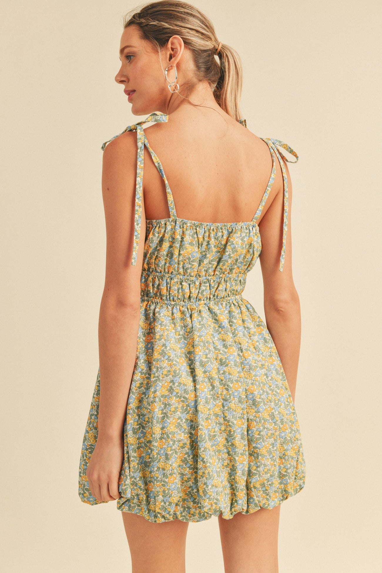 Woman wearing a floral print mini dress with tie straps and smocked waist, back view