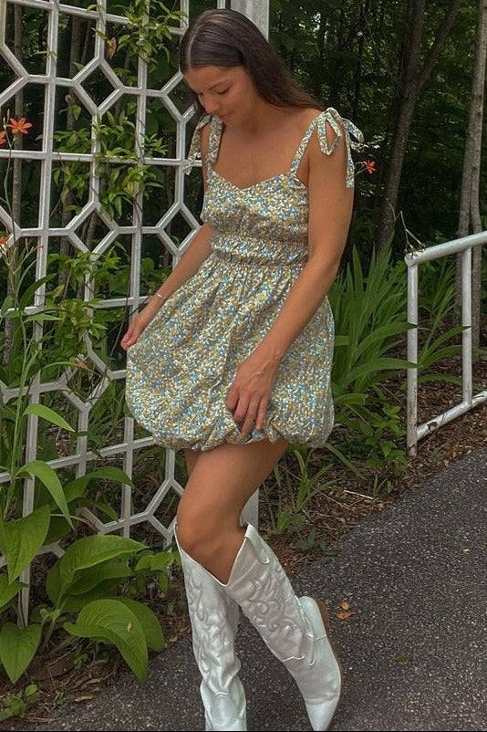 woman wearing a floral mini puff dress with tie straps and white cowboy boots standing outdoors