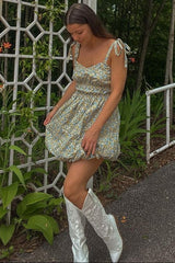 woman wearing a floral mini puff dress with tie straps and white cowboy boots standing outdoors