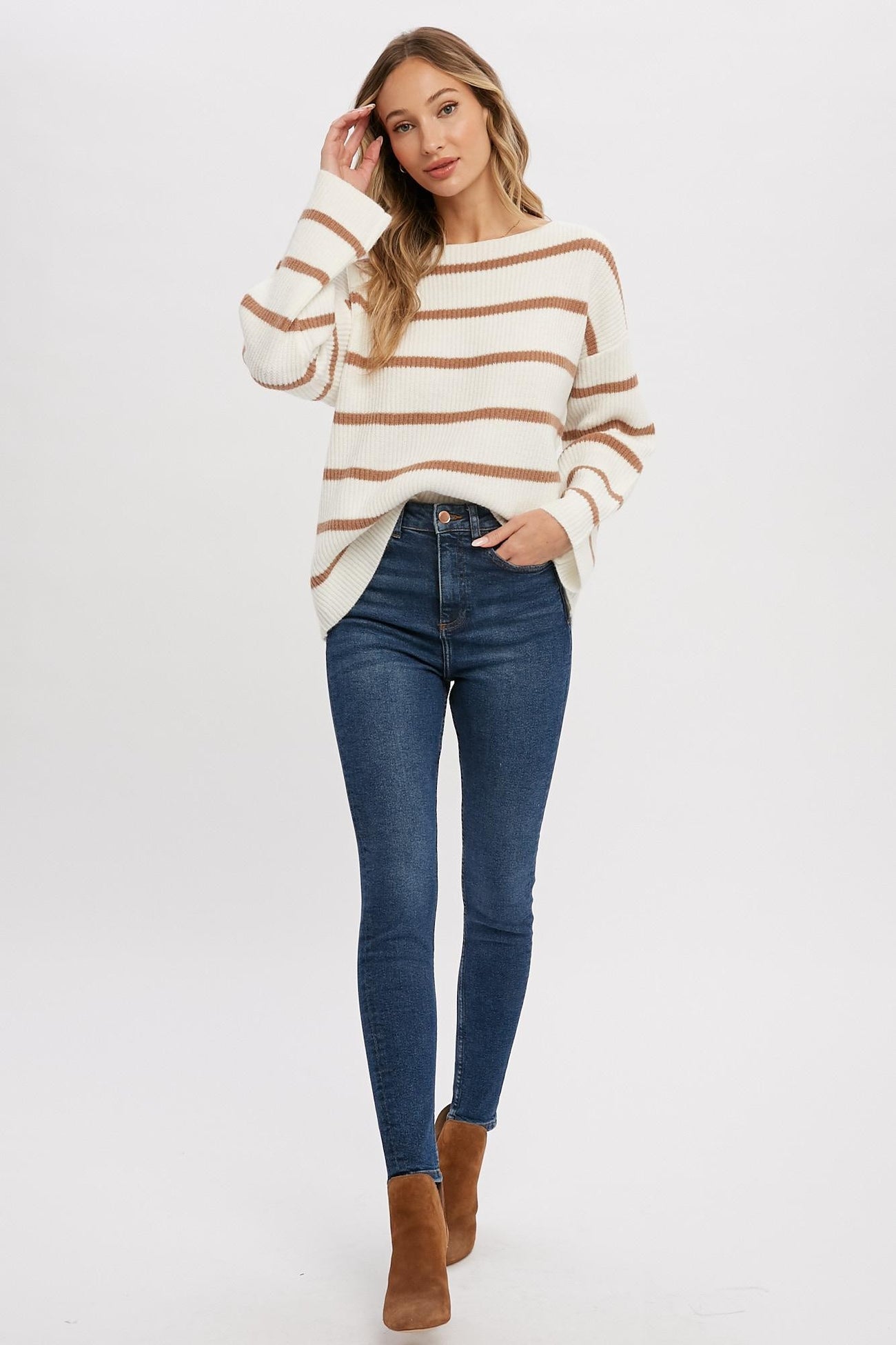 woman wearing white and brown striped oversized sweater with high waisted blue skinny jeans and brown boots