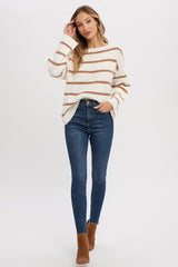 woman wearing white and brown striped oversized sweater with high waisted blue skinny jeans and brown boots