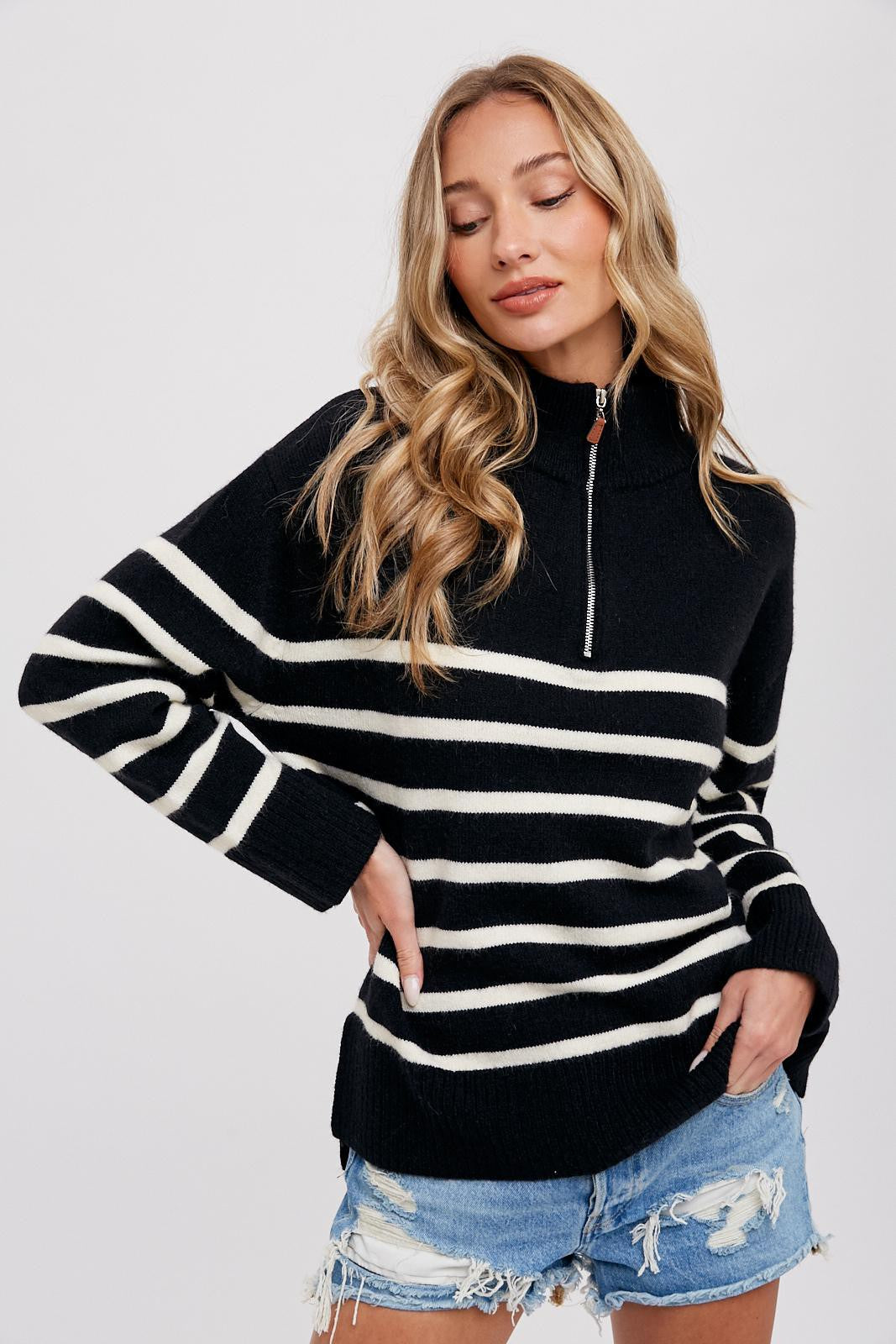 woman wearing a black and white striped quarter-zip sweater and distressed denim shorts