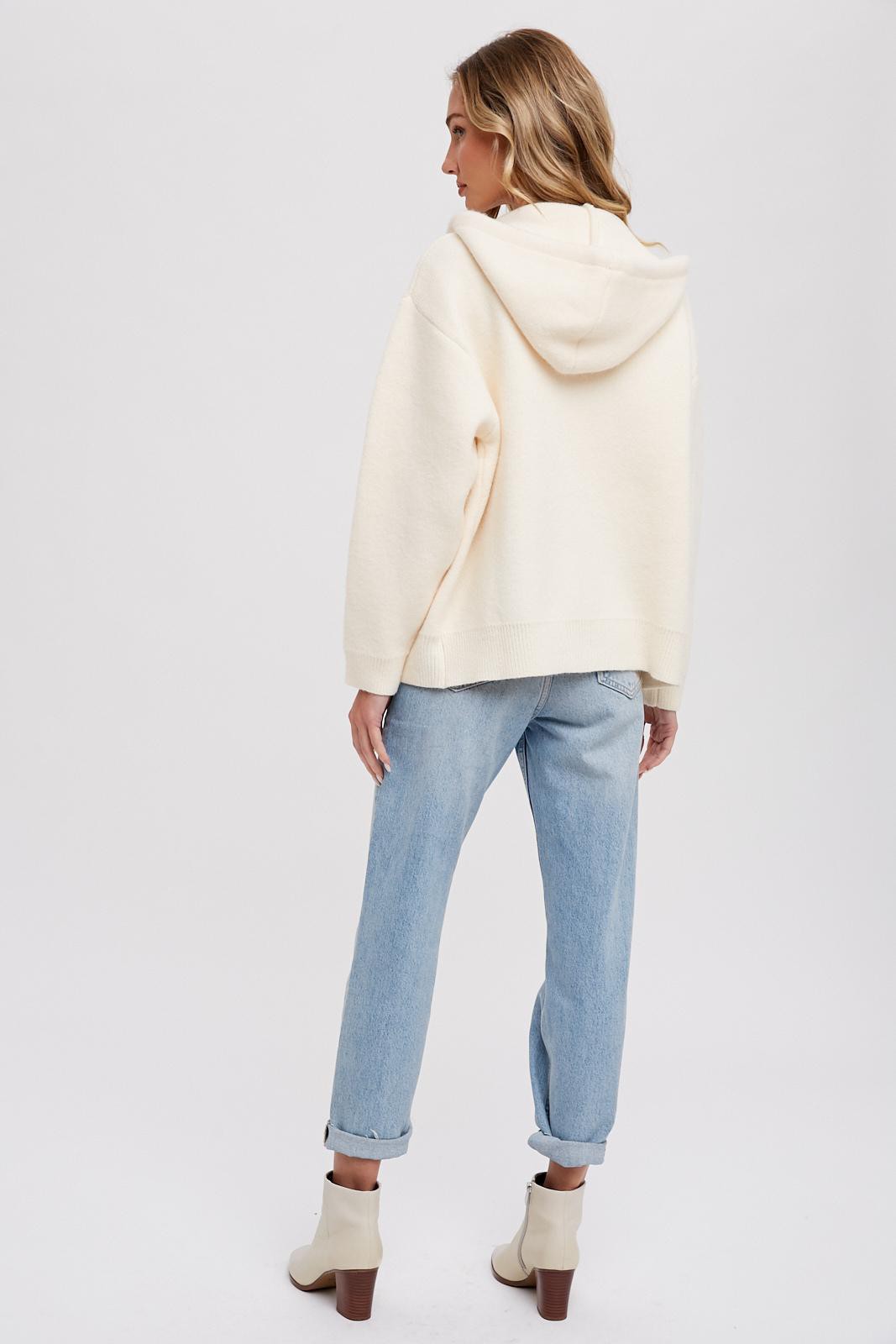 Woman wearing cream oversized knit hoodie and light wash jeans with white ankle boots