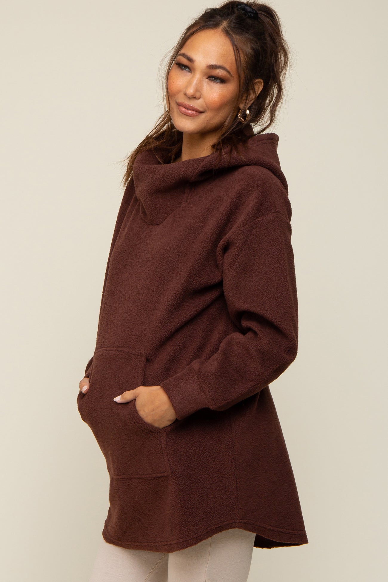 Pregnant woman wearing a brown fleece maternity hoodie with a front pocket and cowl neck