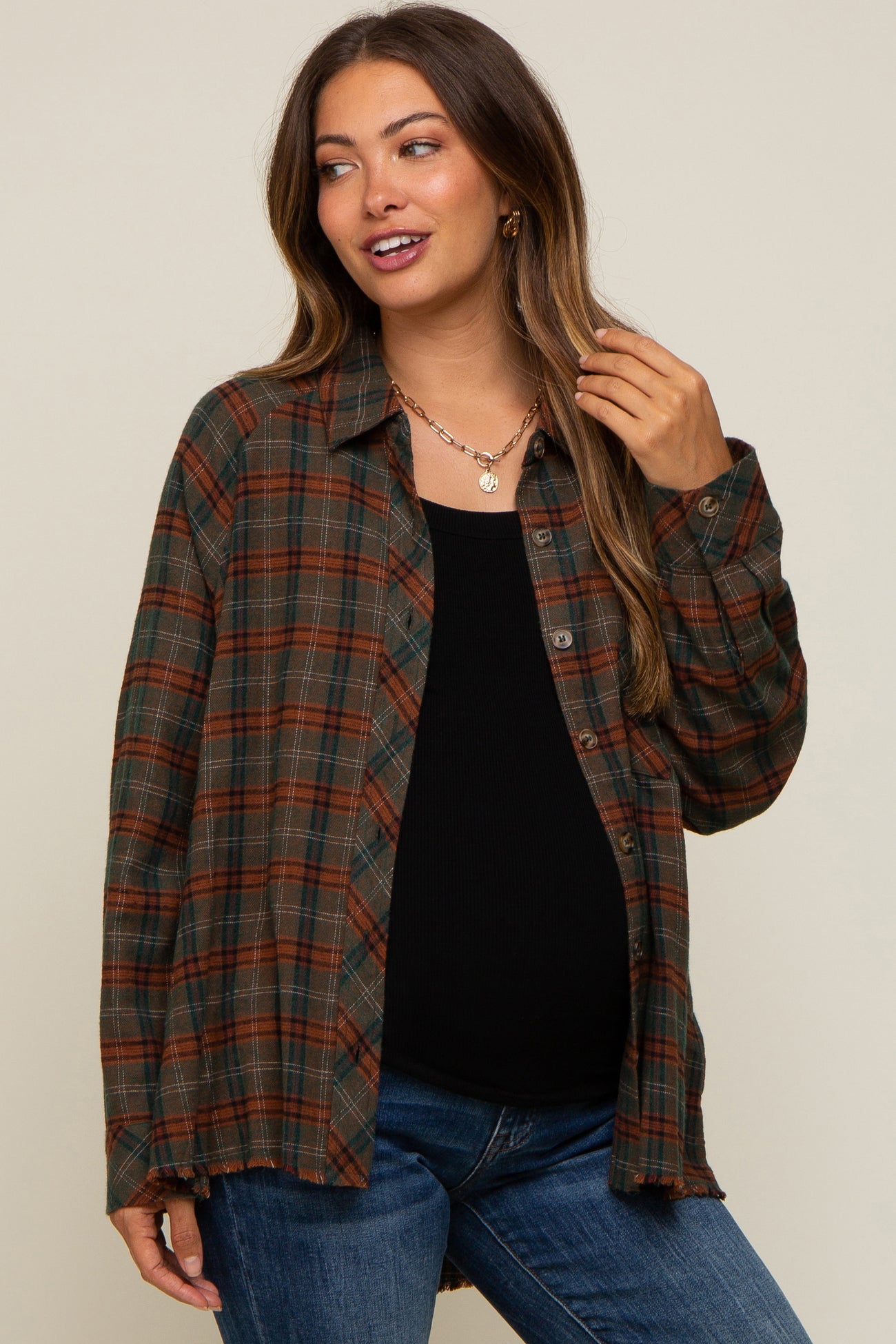 woman wearing an olive and rust plaid flannel shirt over a black maternity top and blue jeans