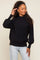 Woman wearing a black mock neck sweater with balloon sleeves and light wash jeans against a neutral background