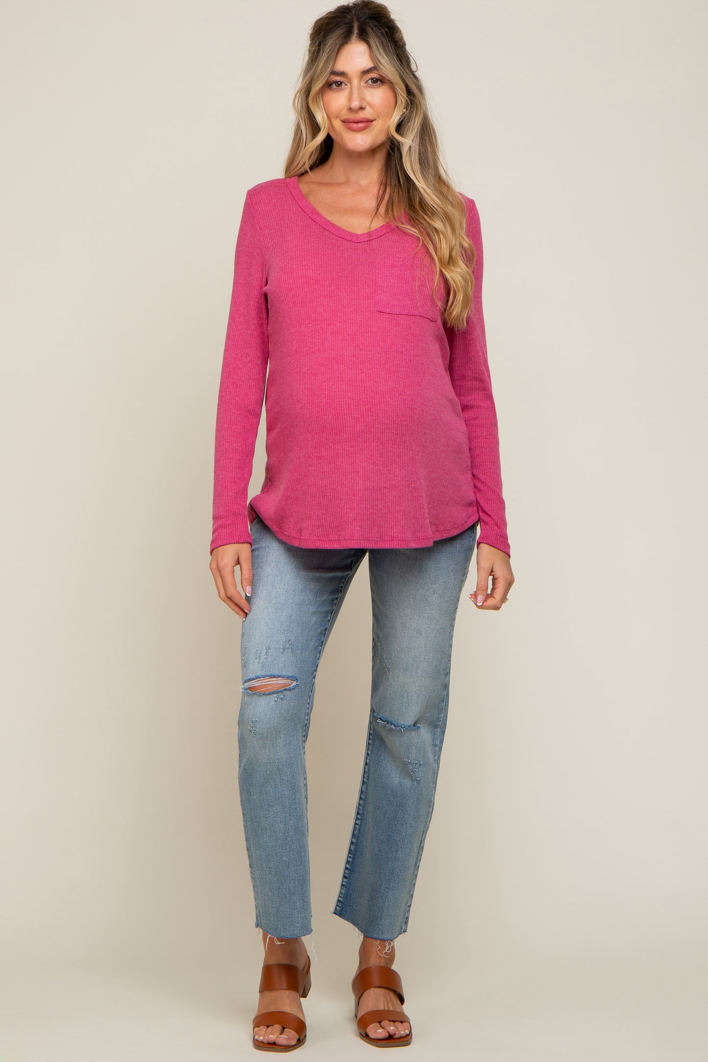 Pregnant woman wearing a pink long sleeve maternity top and distressed blue jeans with brown sandals