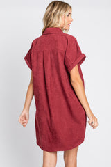 Back view of a woman wearing a burgundy corduroy short sleeve shirt dress with a collar and cuffed sleeves