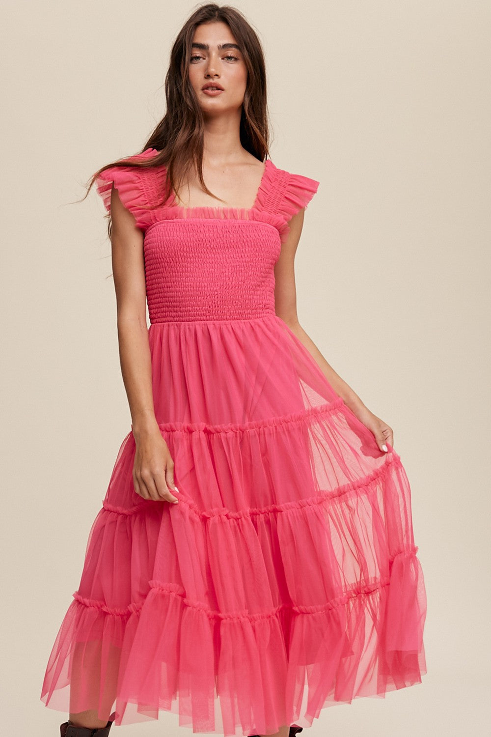 woman wearing a hot pink smocked tulle midi dress with ruffled sleeves and a tiered skirt