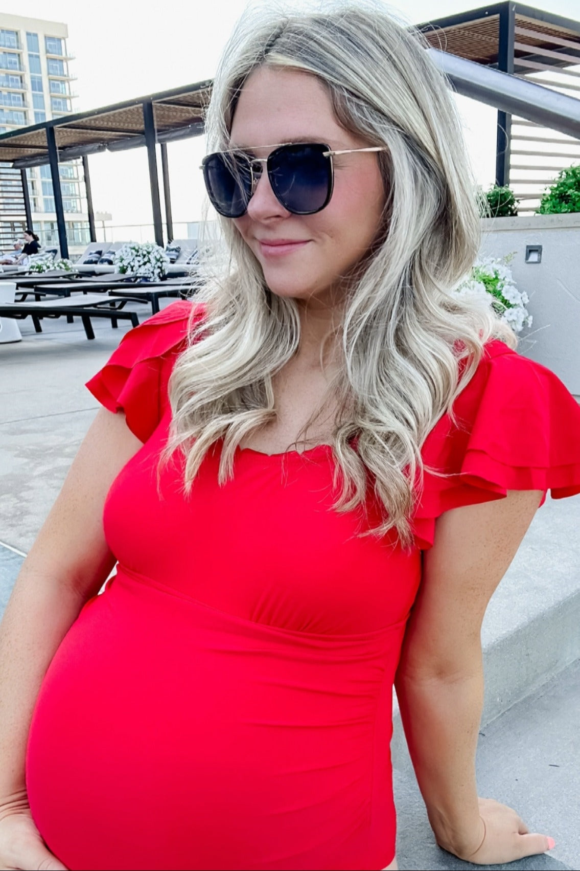 woman wearing a red maternity top with ruffled sleeves and showing her baby bump, accessorized with sunglasses