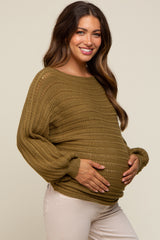 smiling pregnant woman wearing an olive green crochet knit maternity sweater and white pants