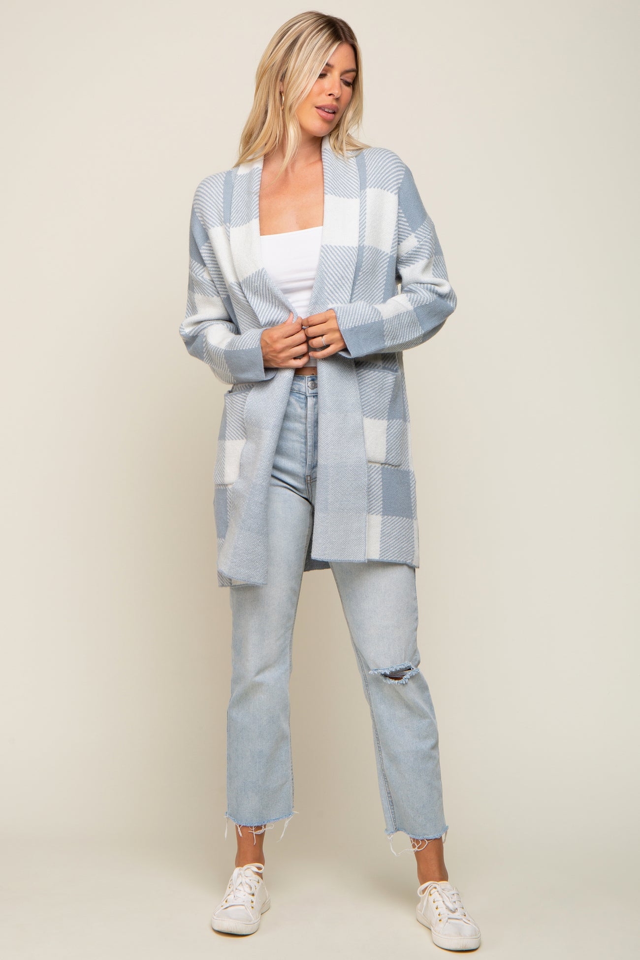 Woman wearing a light blue and white checkered cardigan with distressed jeans and white sneakers