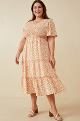 Woman wearing a plus size orange and white floral midi dress with smocked bodice and tiered skirt