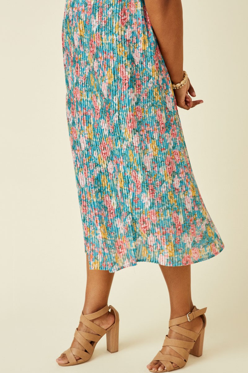 woman wearing a colorful floral pleated midi dress with a fitted bodice and flowy skirt, paired with tan strappy heels