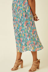 woman wearing a colorful floral pleated midi dress with a fitted bodice and flowy skirt, paired with tan strappy heels