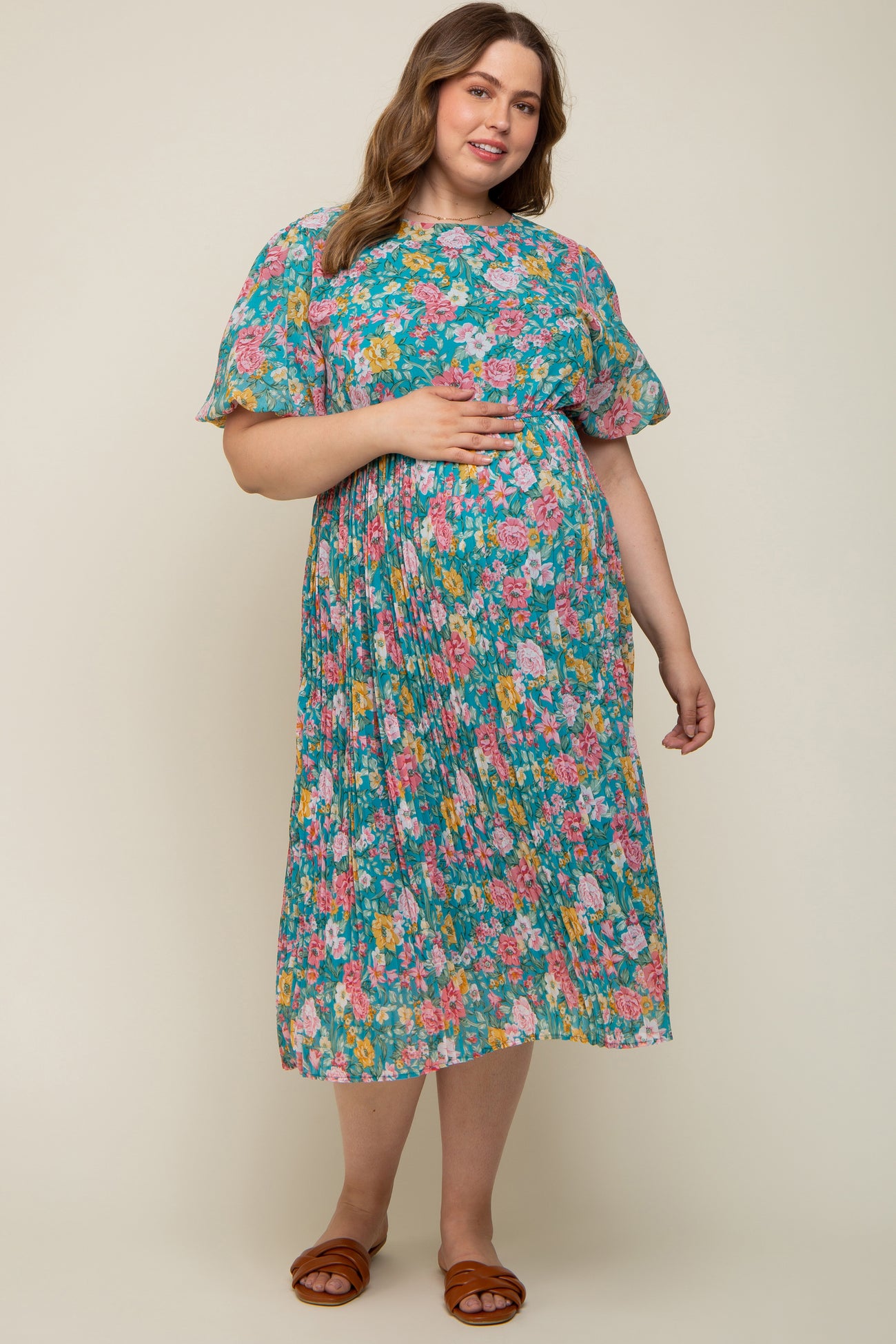woman wearing a floral maternity plus dress in teal with short puff sleeves and holding her baby bump