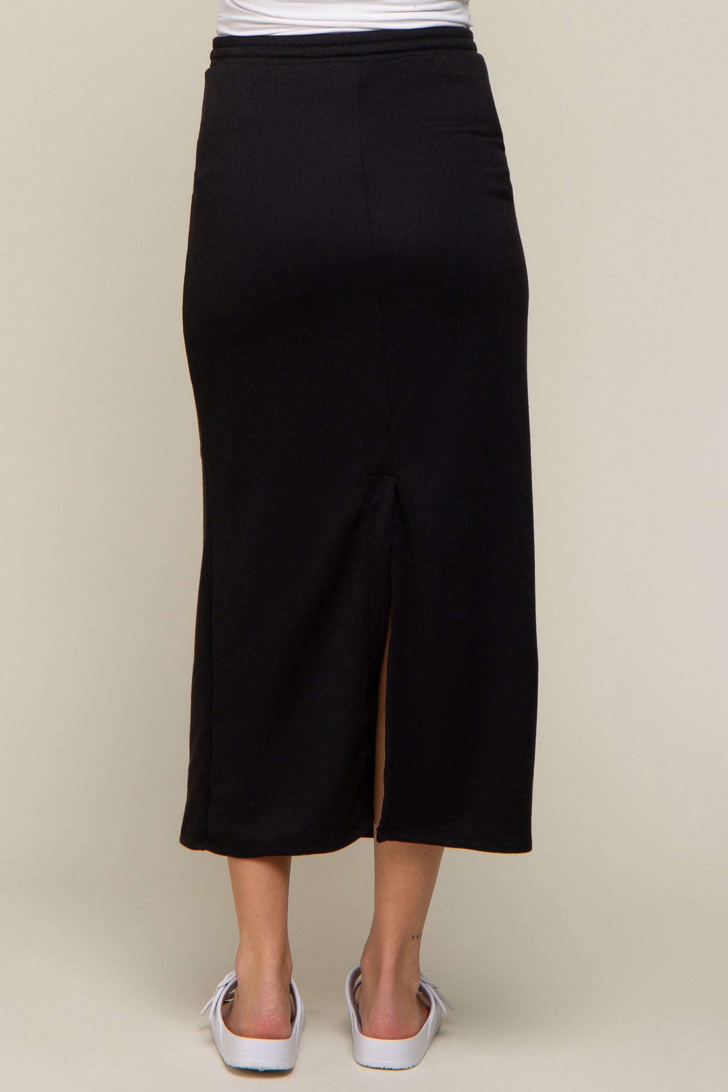 back view of a woman wearing a long black midi skirt with a back slit and white sandals