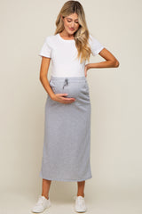 woman wearing a white short sleeve top and a gray maternity skirt, holding her baby bump