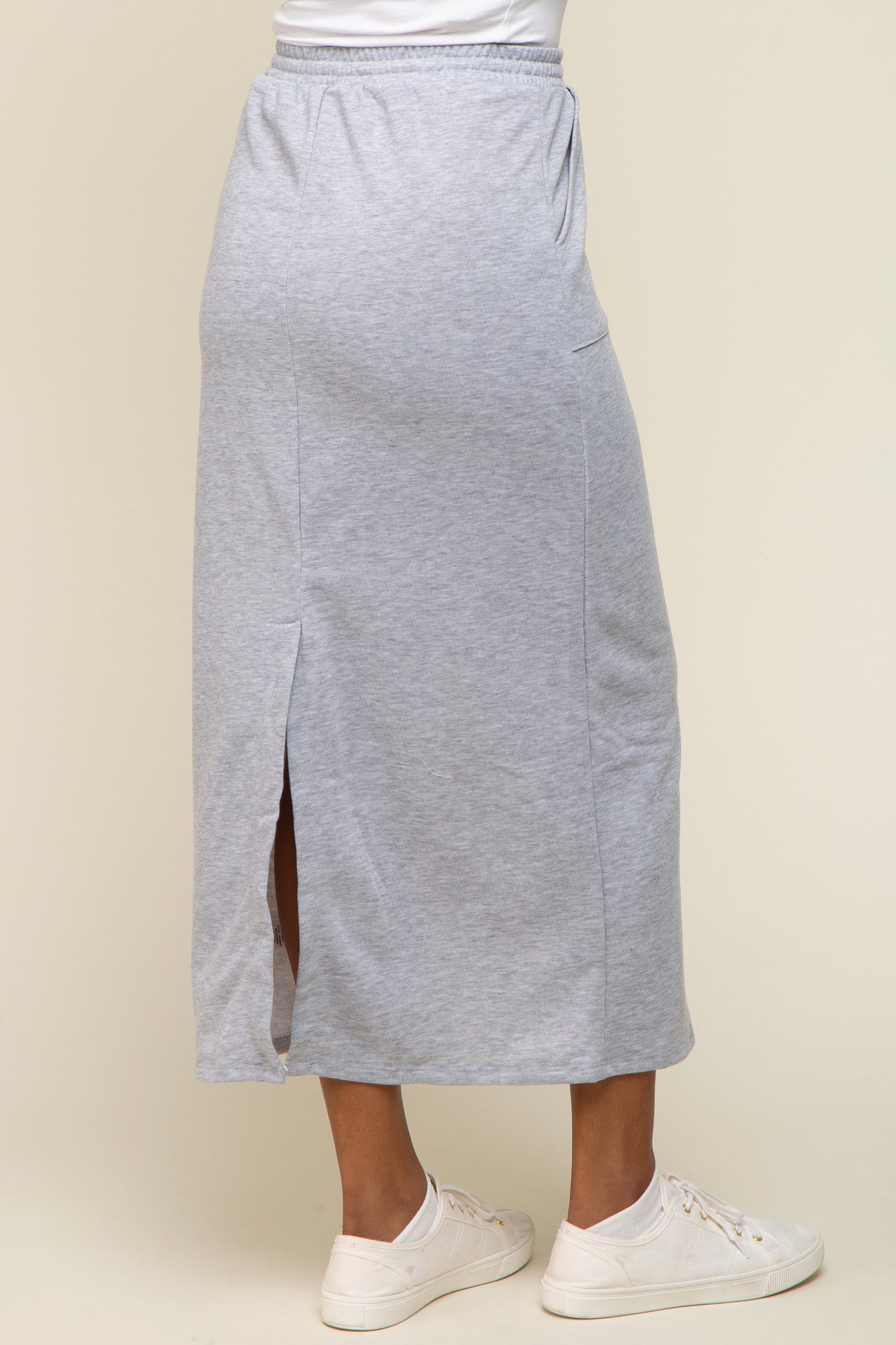 woman wearing a light gray maxi skirt with side slits and a casual fit, paired with white sneakers