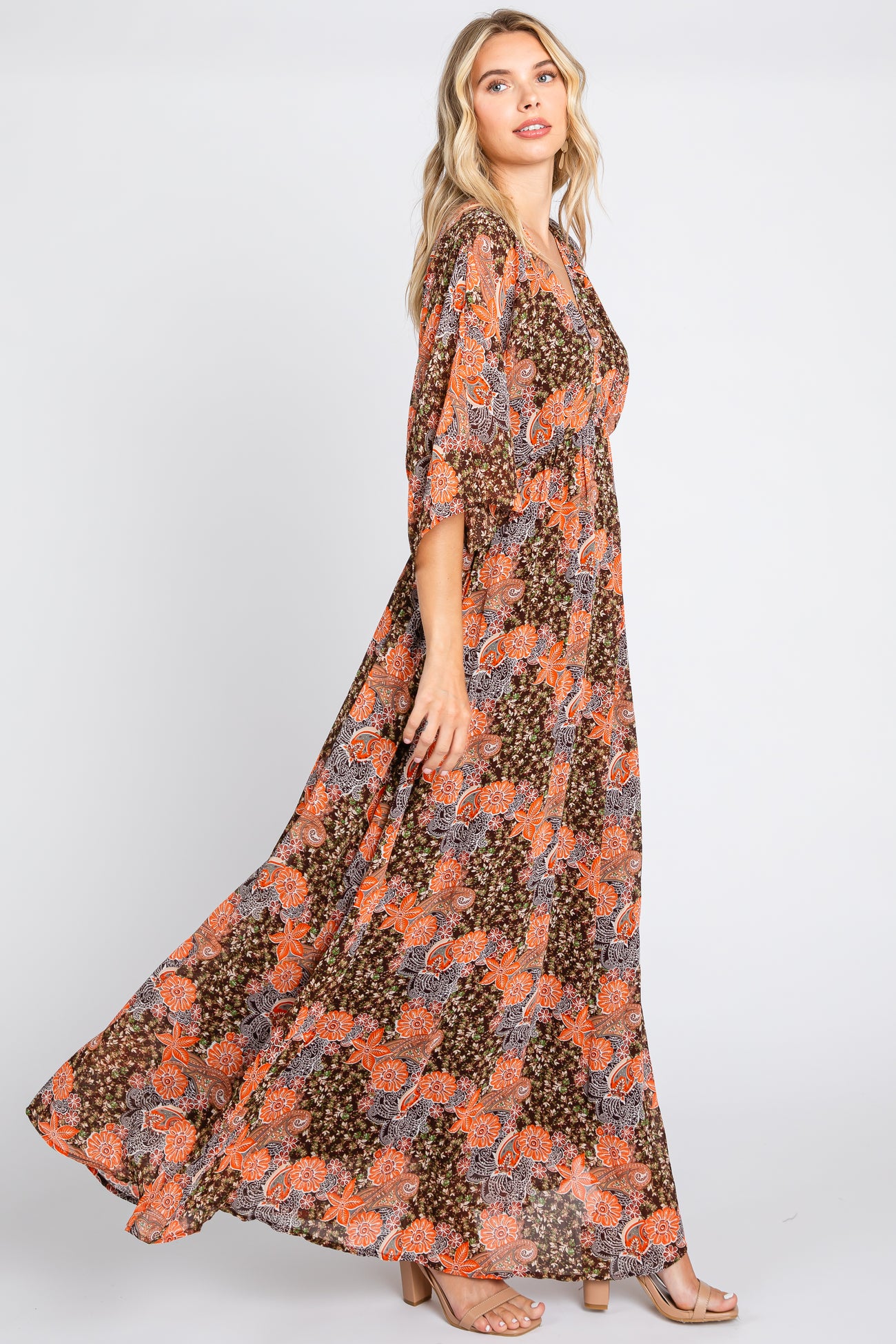 Woman wearing a long brown and orange paisley print maxi dress with flutter sleeves and tan heels