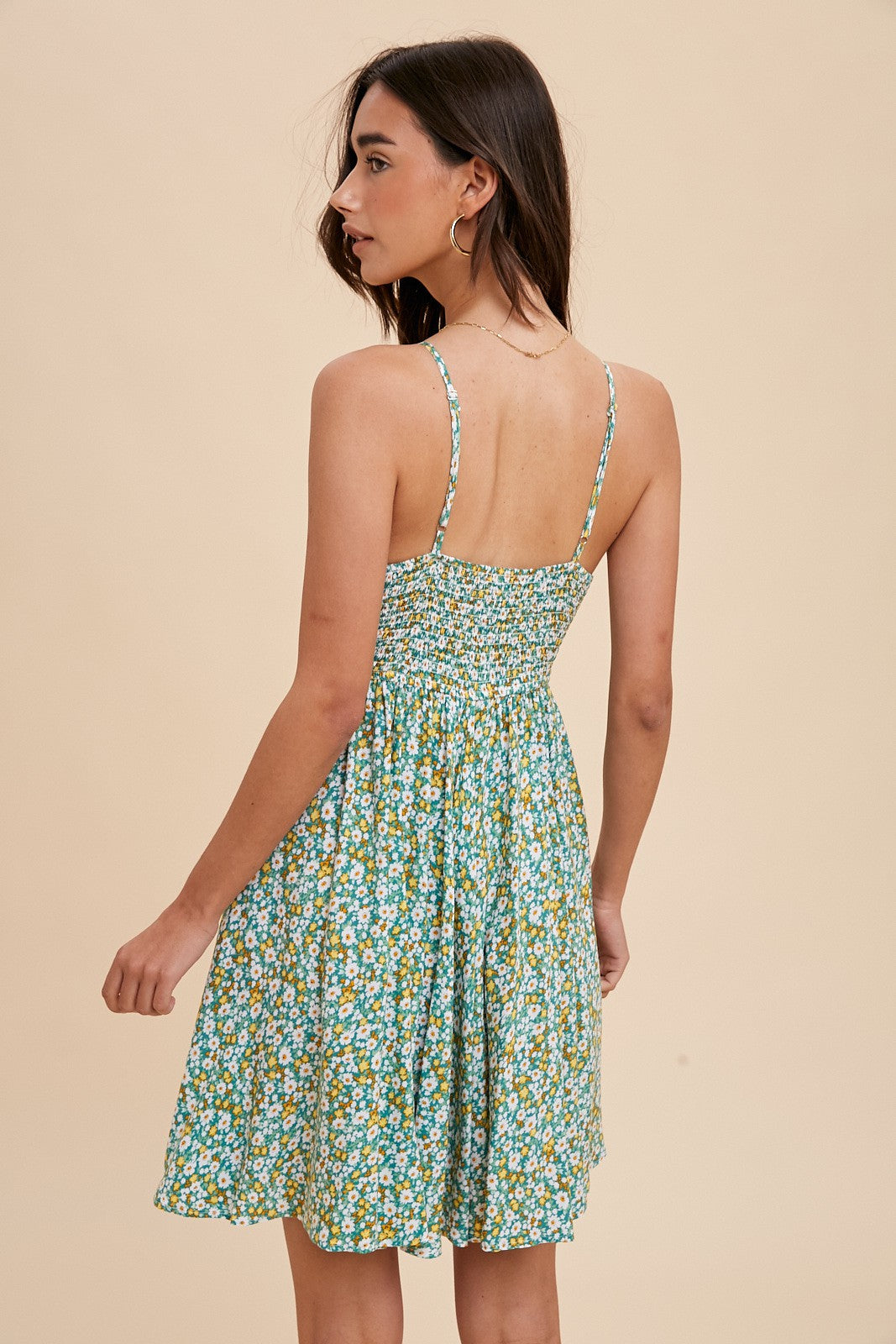 woman wearing a green floral sundress with spaghetti straps and a smocked back, shown from the back