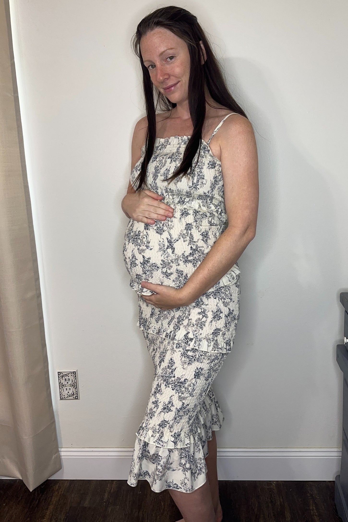 woman wearing a floral maternity dress with a ruffled hemline, gently cradling her baby bump