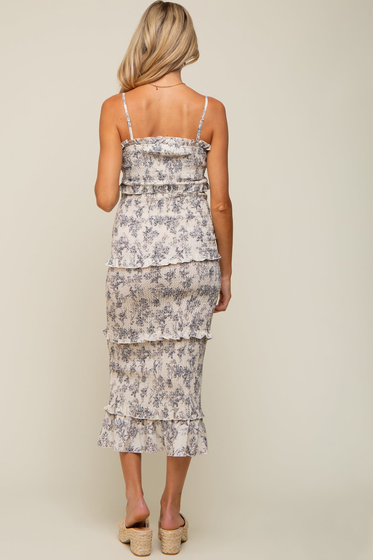 woman wearing a light floral maternity dress with ruffles and adjustable straps, showing a baby bump from the back