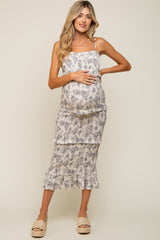 woman wearing a floral maternity dress with ruffles and a visible baby bump, standing and smiling