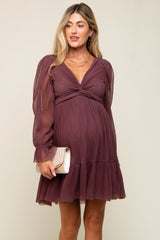 woman wearing a burgundy maternity dress with long sheer sleeves and a tiered ruffle hem, holding a clutch purse and showing her baby bump
