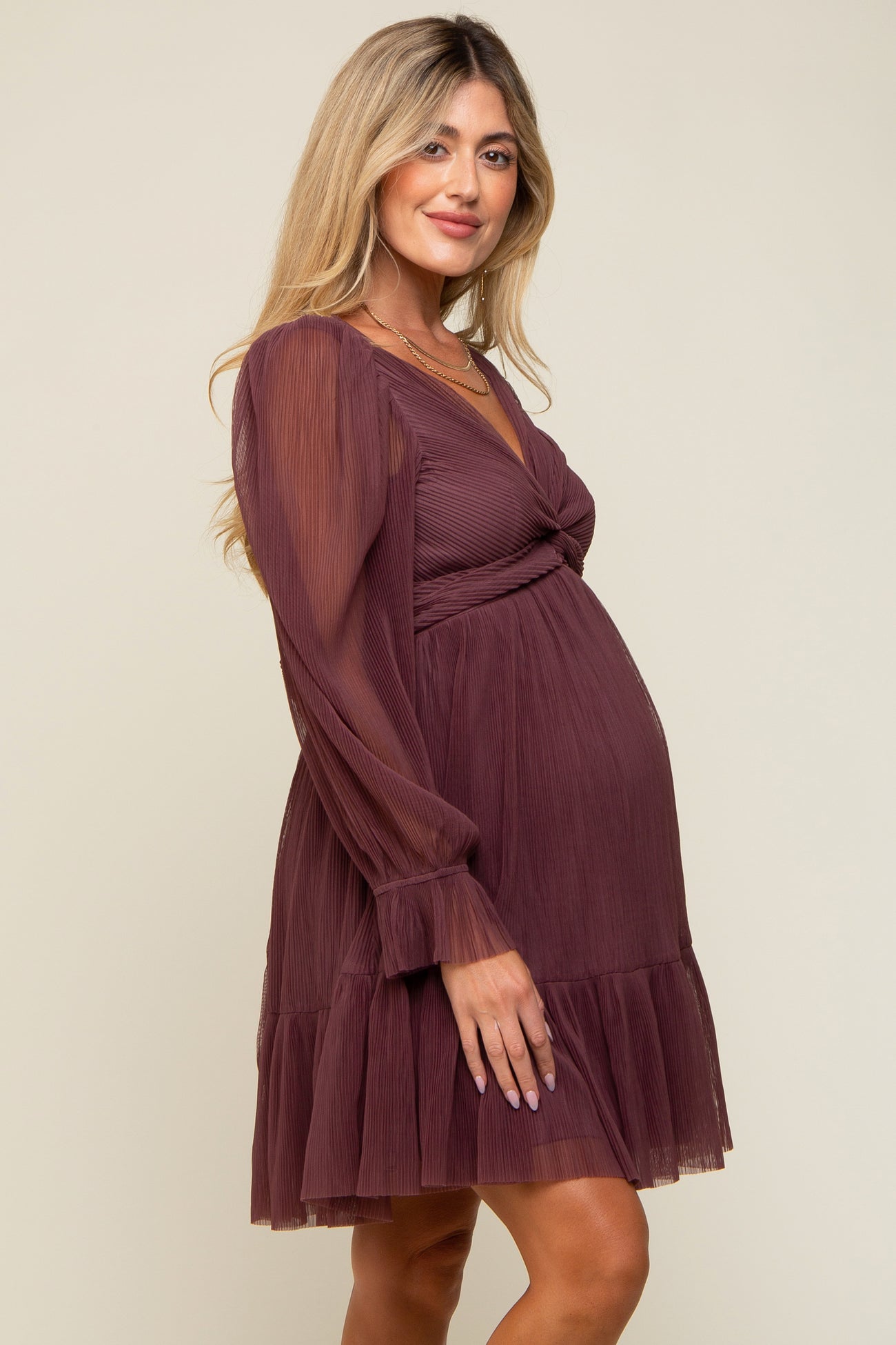 woman wearing a burgundy maternity dress with long sleeves and a ruffled hem, highlighting her baby bump