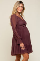 woman wearing a burgundy maternity dress with long sleeves and a ruffled hem, highlighting her baby bump