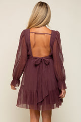 woman wearing a burgundy backless maternity dress with long sleeves and a tie detail at the waist