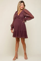 woman wearing a burgundy maternity dress with a v-neck, puff sleeves, and ruffled hem, showcasing her baby bump
