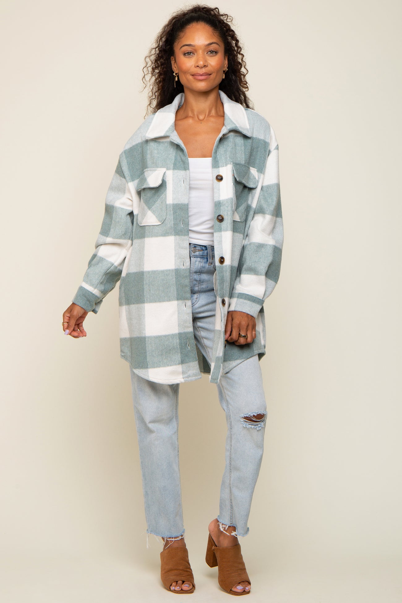 woman wearing a sage green and white plaid shacket with light wash distressed jeans and brown mules
